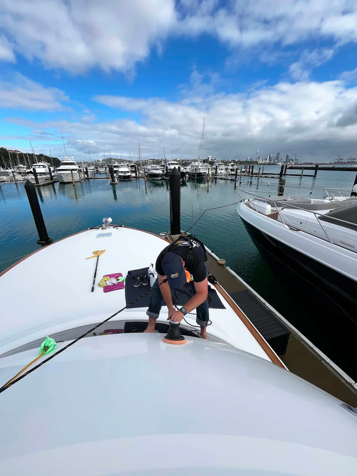 George machine-polishing a boat foredeck with the Auckland skyline behind — Hull Yeah Detailing